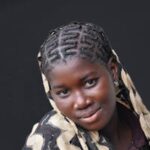 Portrait of a smiling young woman with braided hair against a dark background.